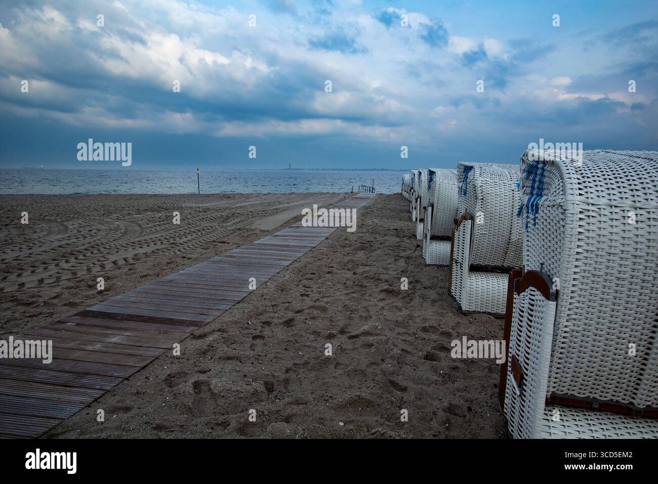 Liegestühle wie in deutschland üblich in einer Reihe unter einem Gehweg aus Holzdielen mit bewölktem Himmel an Nord- oder ostseeküste Stockfoto