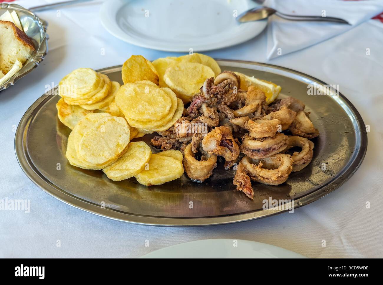 Eine Platte mit traditionellen gebratenen Calamari (Tintenfischringe) und Kartoffeln, ein beliebtes mediterranes Meeresfrüchte-Gericht, das in einem Restaurant serviert wird Stockfoto
