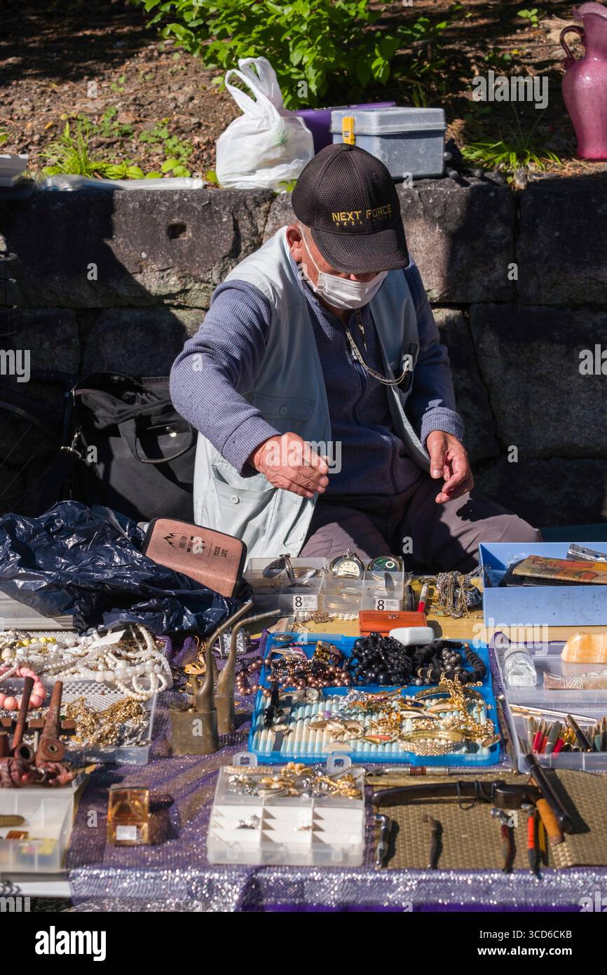 Männlicher Verkäufer, der Schmuck und verschiedene Kleinteile während des monatlichen Flohmarktes am Tenmangu-Schrein, Bakurocho, Kamigyo Ward, Kyoto, Kansai, verkauft. Honshu, Stockfoto
