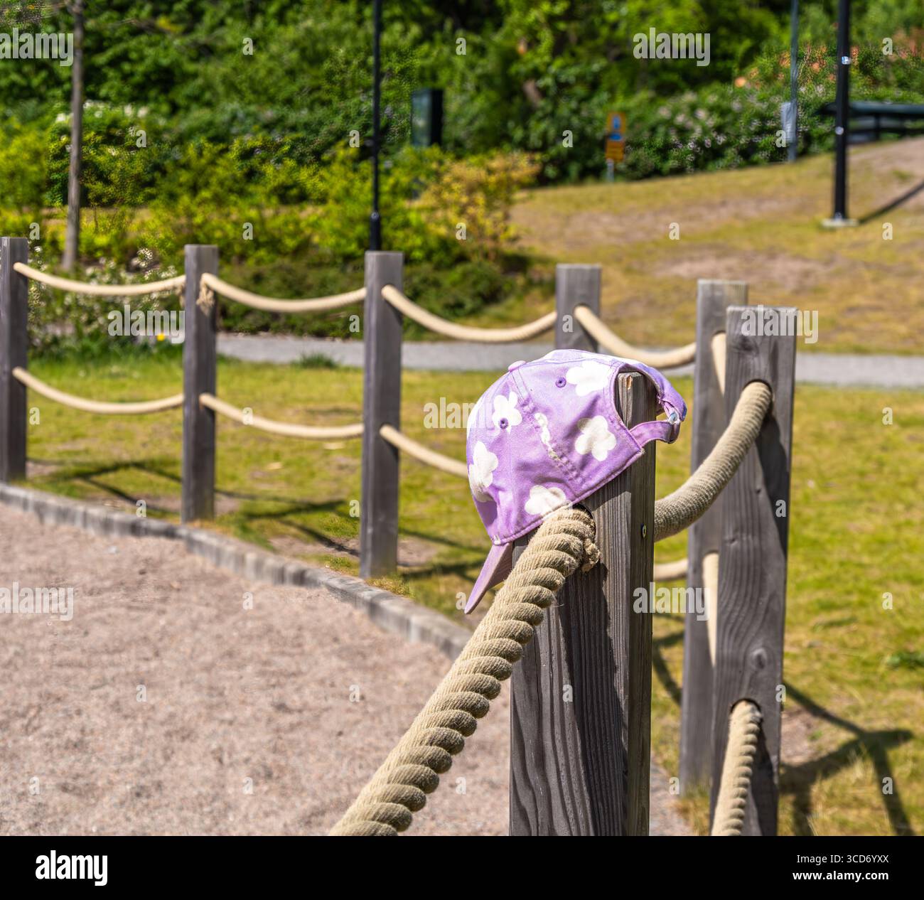Eine violette Blumenkappe hängt an einem Holzpfosten mit Seilzäunen in einem sonnigen Park. Stockfoto Eine violette Blumenkappe hängt an einem Holzpfosten mit Seilzäunen in einem sonnigen Park. Stockfoto