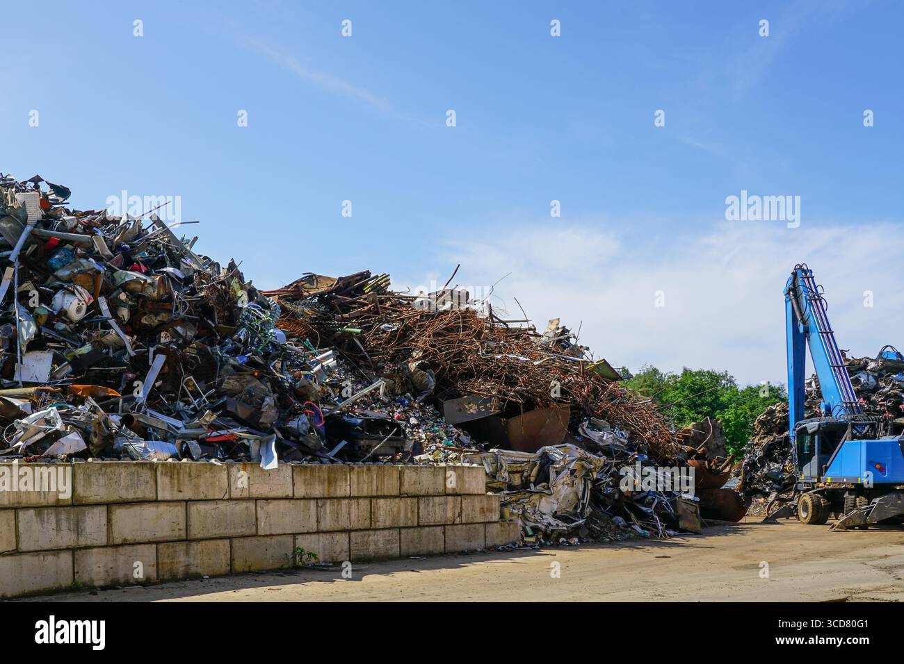 Industrieschrottplatz mit großen Stapeln recycelbarer Eisen- und NE-Metalle und einem blauen Kran zum Sortieren und Verladen von Materialien Stockfoto