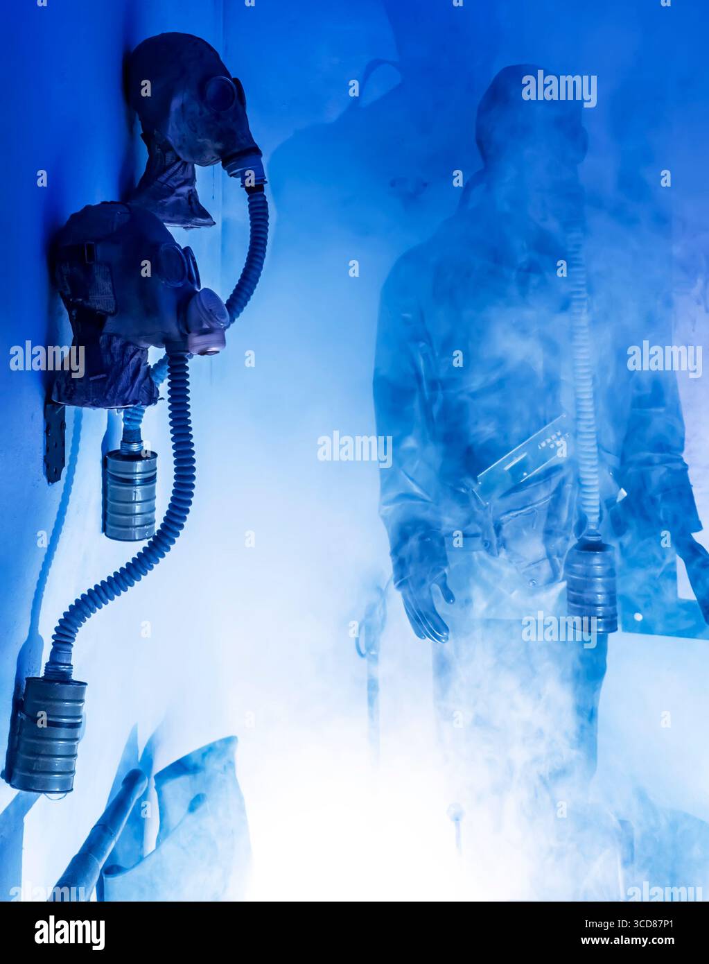 Gasmasken und eine Figur in einem rauchigen, blau beleuchteten Raum. Stockfoto
