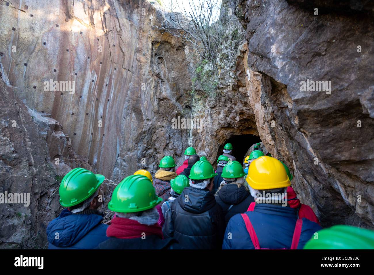 Eine Gruppe von Menschen, die grüne und gelbe Helme tragen, betreten eine Höhle oder einen Tunnel, umgeben von felsigen Wänden Stockfoto