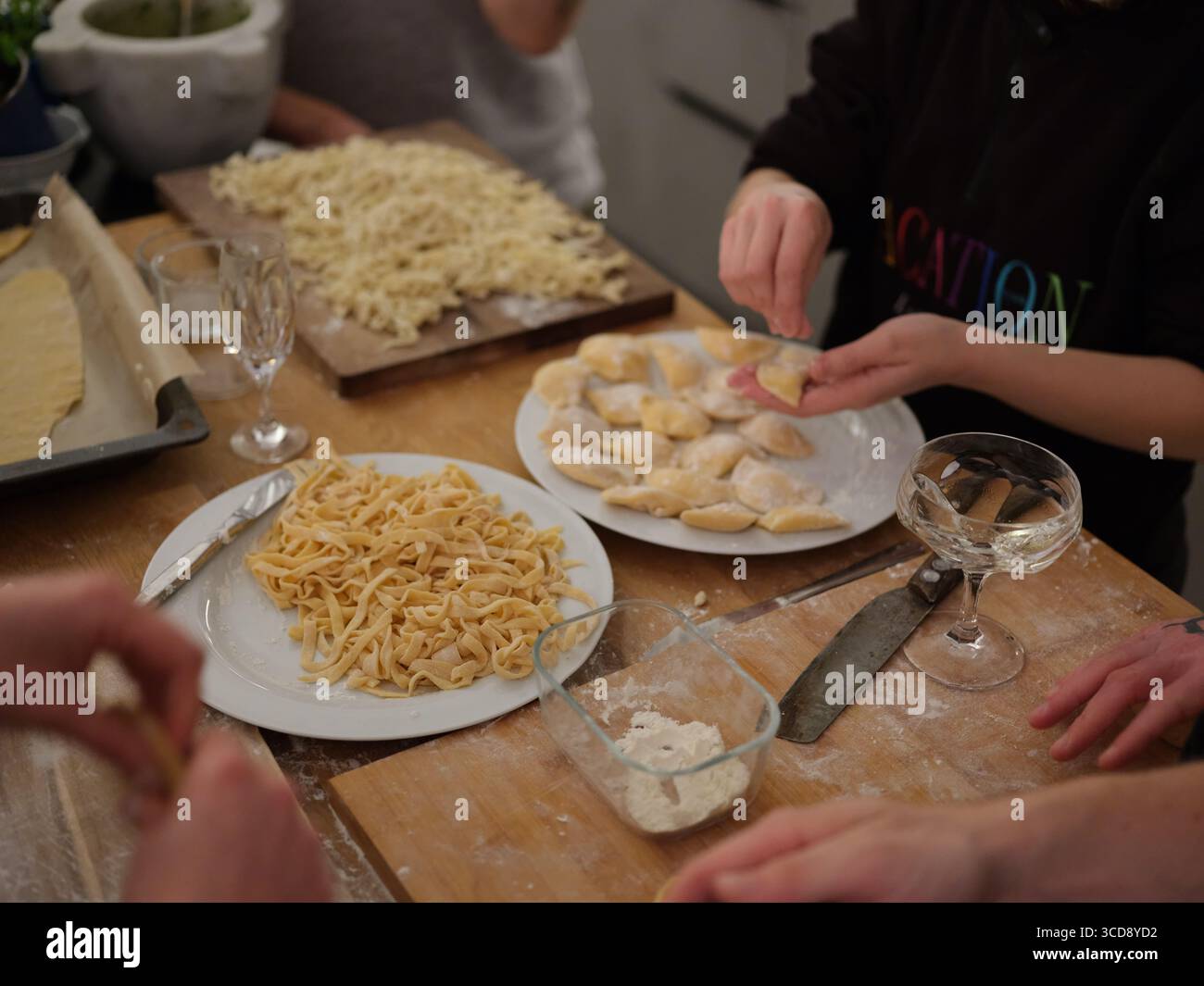 Gruppe von Menschen, die frischen Teig von Hand in der Küche zubereiten, Nahaufnahme des Kochprozesses, kulinarische Kunst und traditionelle Nudelherstellung. Stockfoto