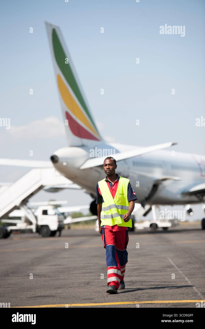 Mitarbeiter der Bodenbesatzung am Flughafen in Sicherheitsweste, die auf der Landebahn in der Nähe von Flugzeug, Flugbetrieb, Reiseindustrie, Flugzeugpersonal, Transportservice laufen Stockfoto