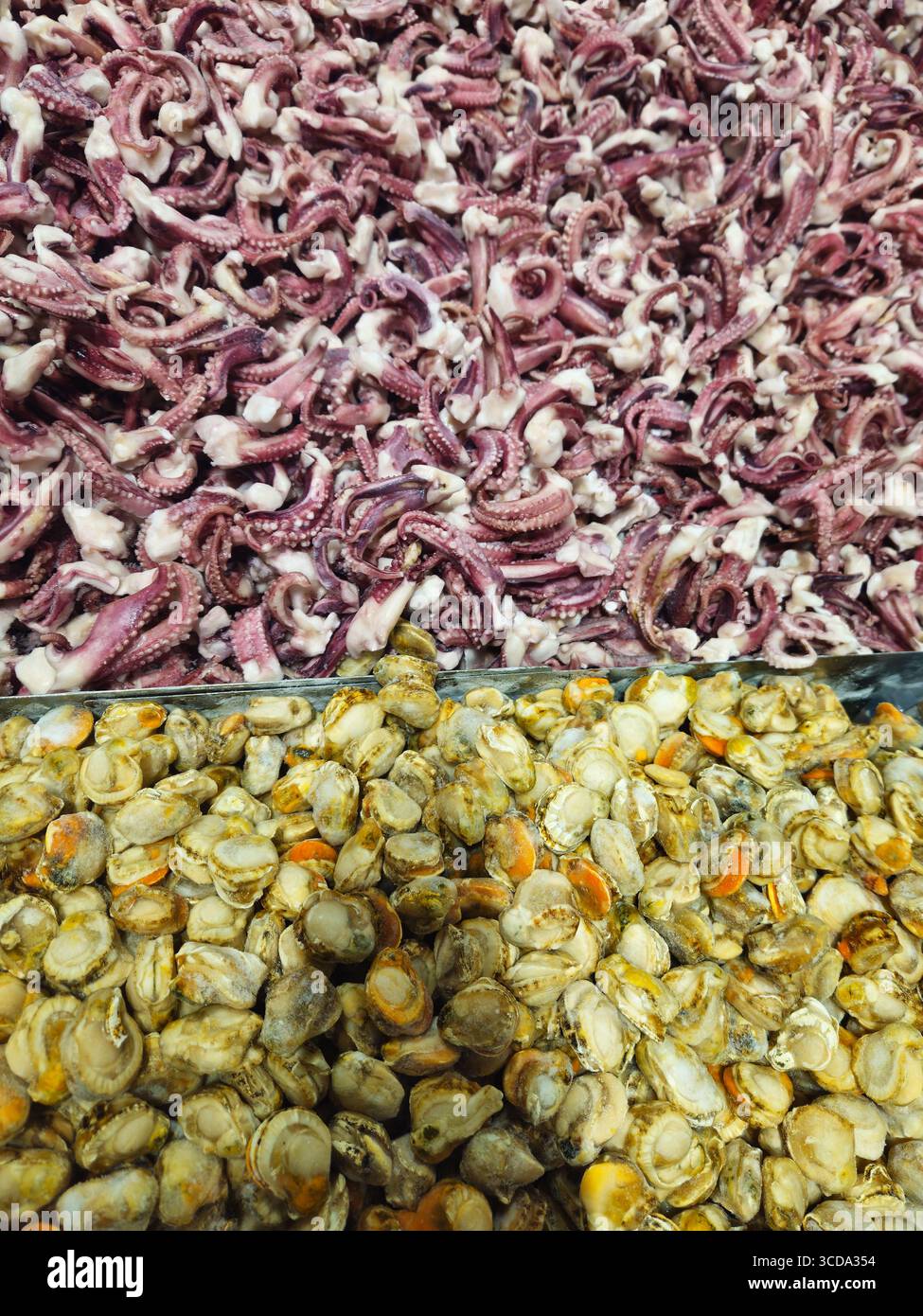 Nahaufnahme von gefrorenen Kraken-Tentakeln und Muschelfleisch, die nebeneinander in Edelstahlschalen auf einem chinesischen Meeresfrüchtemarkt gezeigt werden Stockfoto