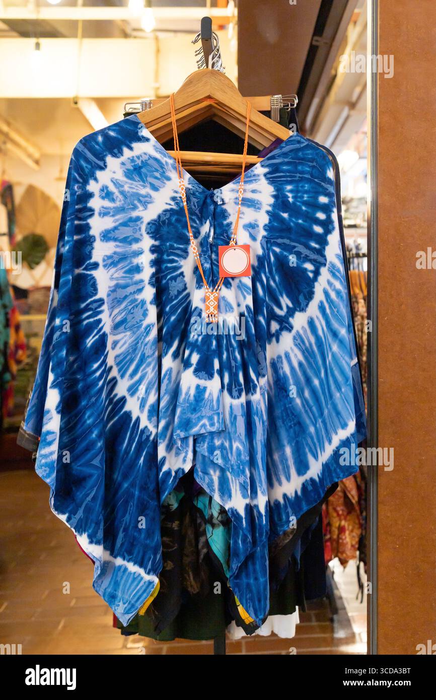 Ein leuchtend blauer Poncho mit Bindegürtel befindet sich in einem stilvollen Modegeschäft auf einem Holzbügel und zeigt komplizierte Designs. Stockfoto