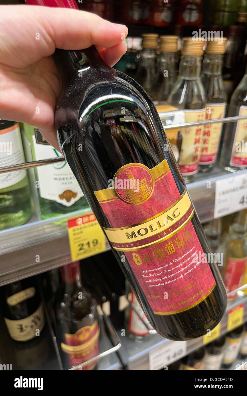 Eine Hand nimmt eine Flasche Rotwein aus dem Regal eines Supermarktes Stockfoto