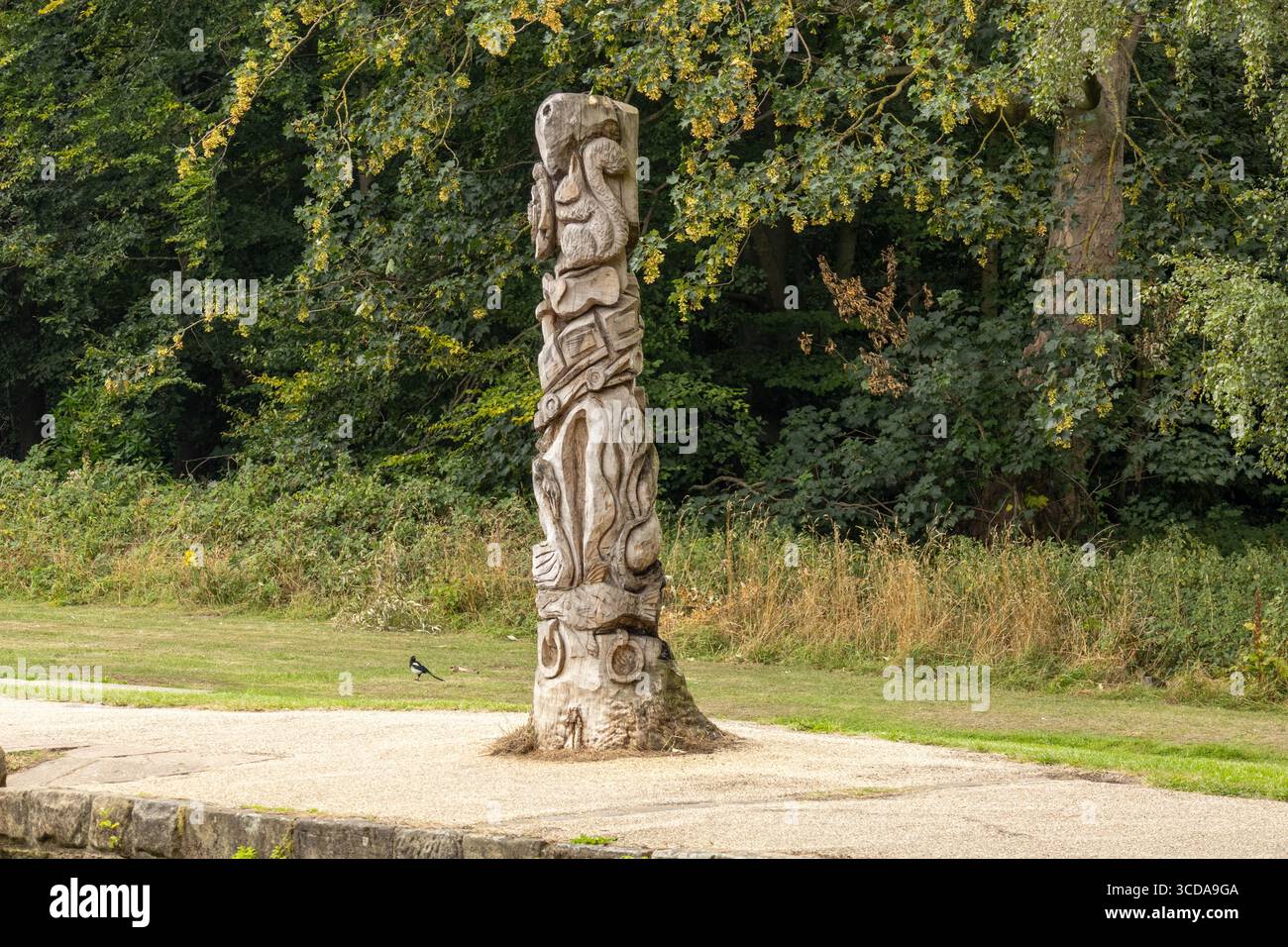Vertikaler geschnitzter Totempfahl aus Holz, der in einem grasbewachsenen Park mit Bäumen im Hintergrund steht Stockfoto
