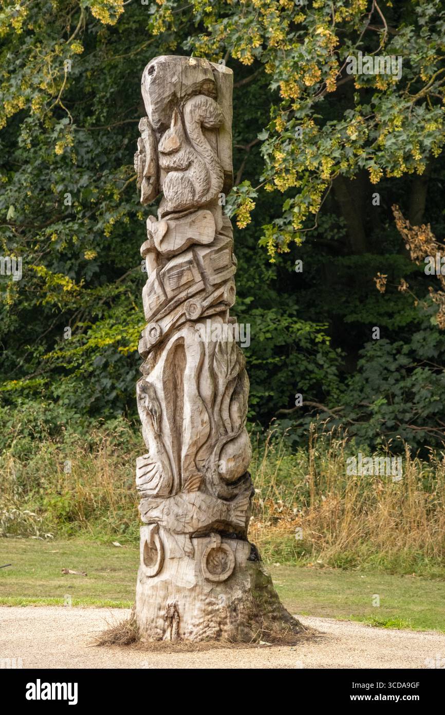 Vertikaler geschnitzter Totempfahl aus Holz, der in einem grasbewachsenen Park mit Bäumen im Hintergrund steht Stockfoto