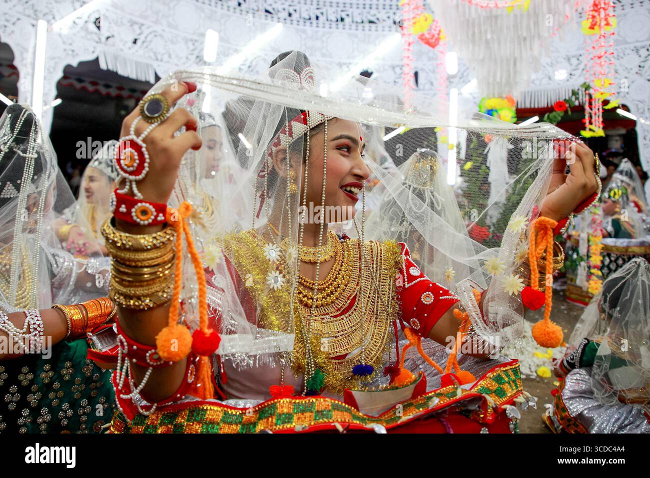 Sylhet, Bangladesch - 08. November 2022: Blick auf eine strahlende, lächelnde Frau, die in traditionellen roten und goldenen Gewändern gehalten wird, die in einer festlichen Feier einen klaren Schleier hält. Stockfoto