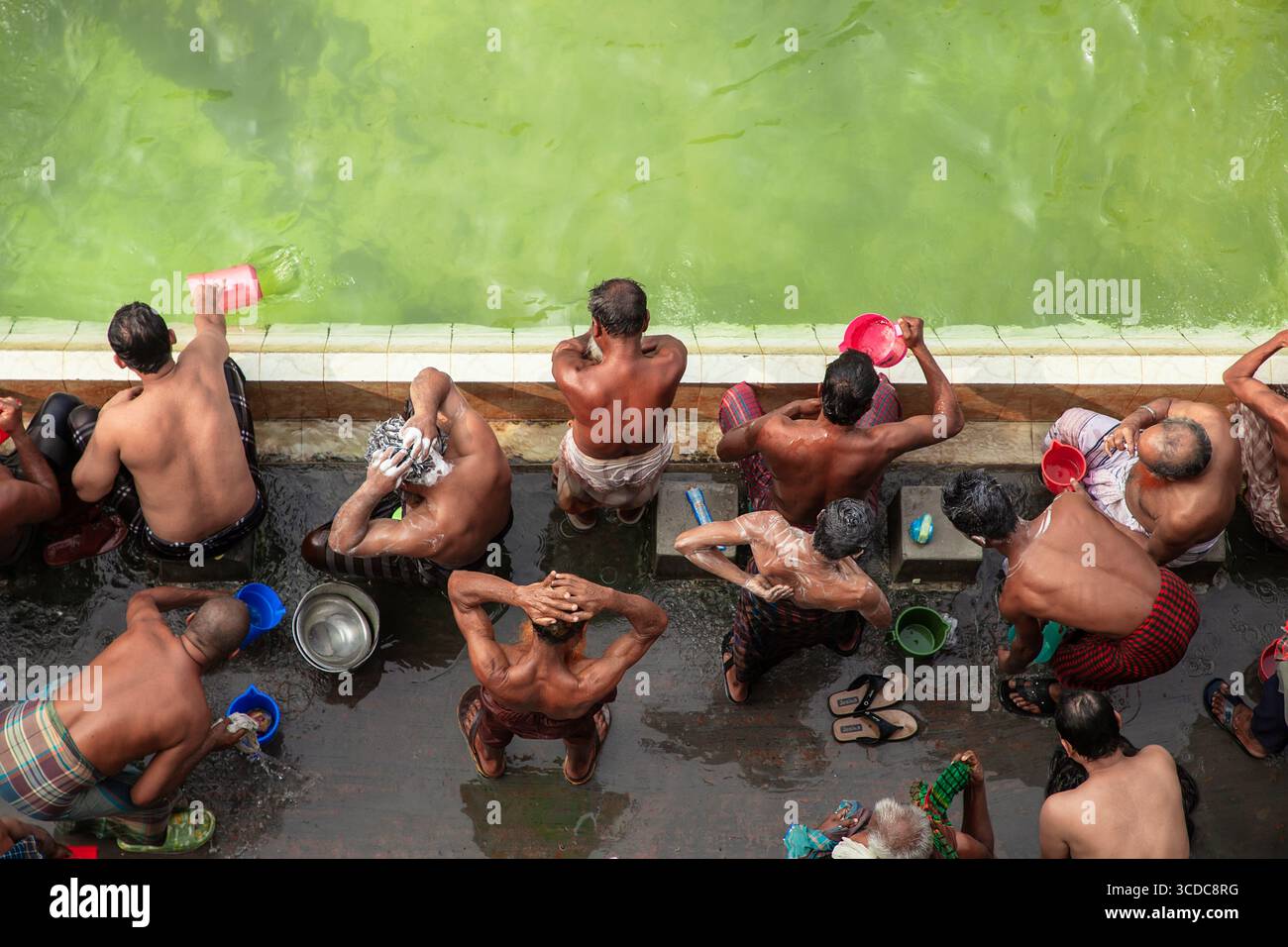 Tongi, Bangladesch - 31. Januar 2025: Aus der Vogelperspektive von Männern, die sich am schimmernden, jadegrünen Wasserrand baden und reinigen, ihre Haut glitzert Stockfoto
