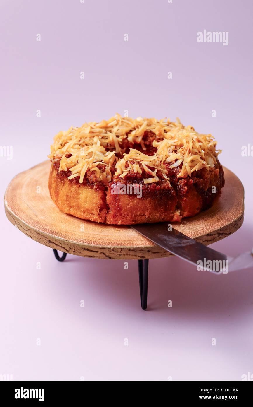 Ein frisch gebackener Kuchen mit gerösteten Kokosflocken und einer reichhaltigen Füllung, mit einem Kuchenheber, der auf einem rustikalen Holzständer in die Seite gesteckt wird Stockfoto
