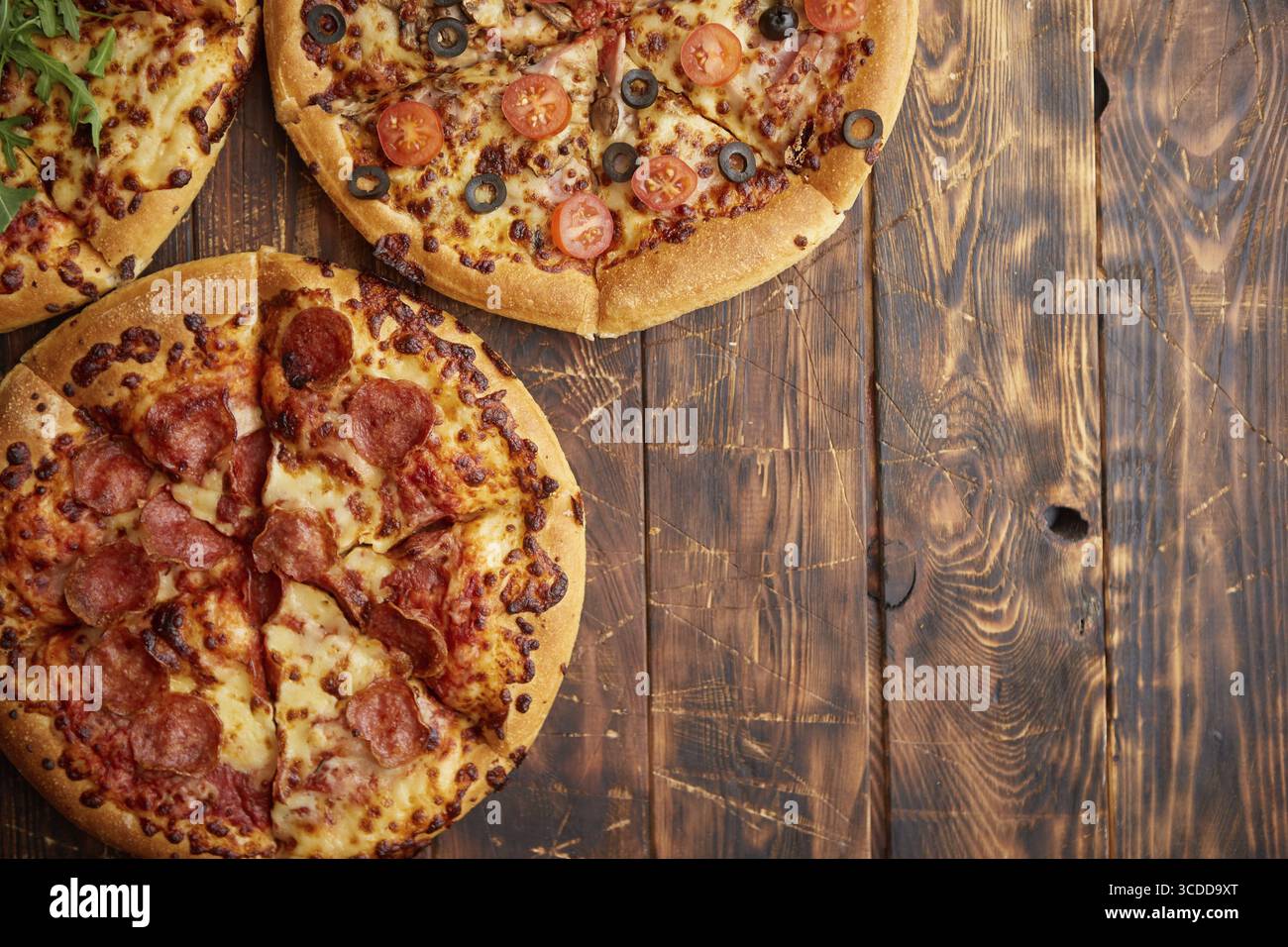 Komposition von drei verschiedenen Pizzen auf einem rostigen, zerkratzten Holztisch. Warme und frische Speisen, die verzehrfertig sind Stockfoto