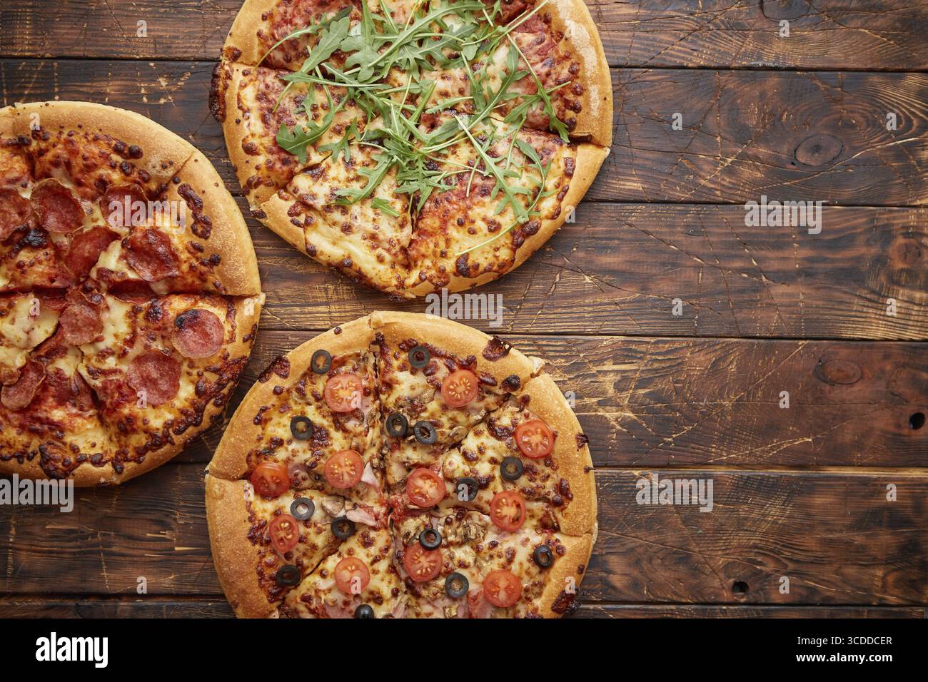 Komposition von drei verschiedenen Pizzen auf einem rostigen, zerkratzten Holztisch. Warme und frische Speisen, die verzehrfertig sind Stockfoto