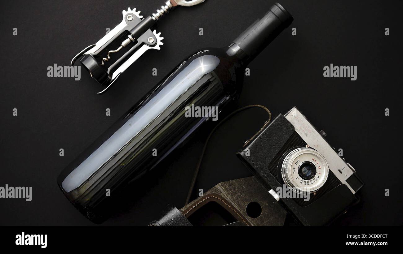 Rotweinflasche, Korkenzieher und alte Fotokamera auf schwarzem mattem Hintergrund. Draufsicht mit Kopierbereich Stockfoto