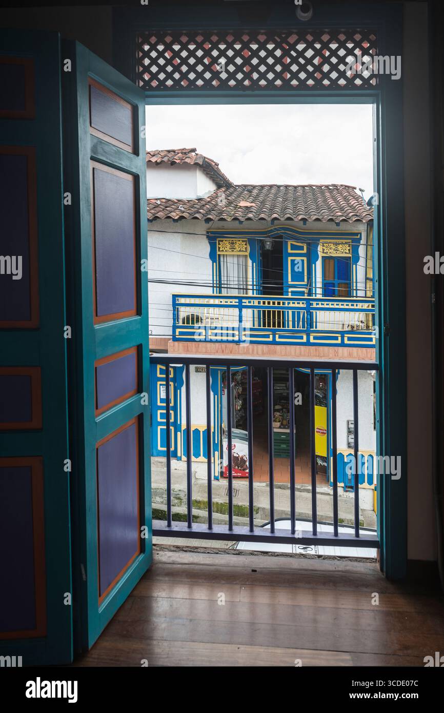Blick durch geöffnete Tür auf die gegenüberliegende Straßenseite: Farbenfrohes Haus mit Balkon und Geschäft. Salento, Departement Quindío, Kolumbien Stockfoto