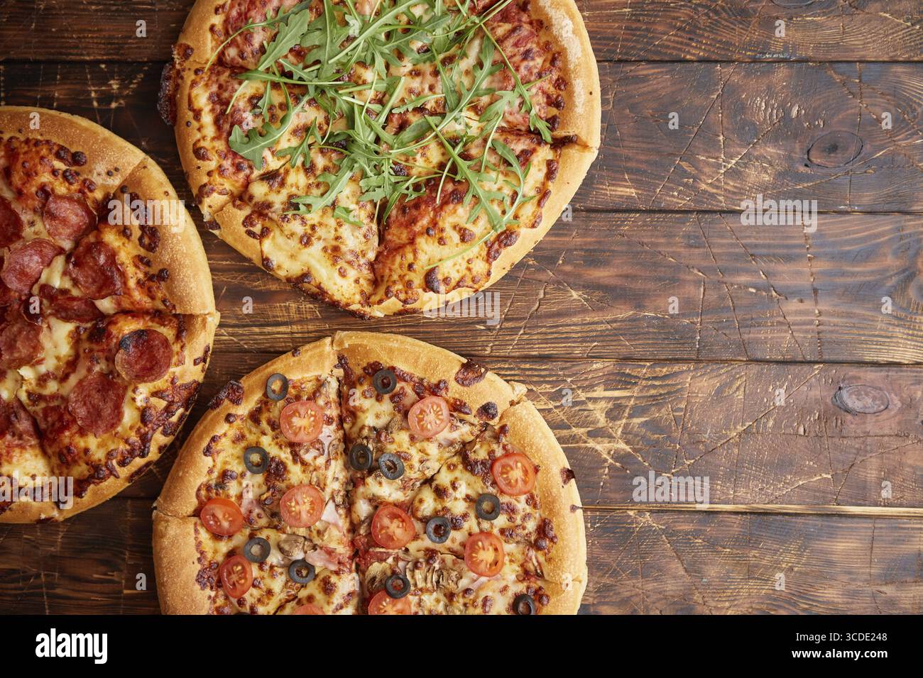 Komposition von drei verschiedenen Pizzen auf einem rostigen, zerkratzten Holztisch. Warme und frische Speisen, die verzehrfertig sind Stockfoto