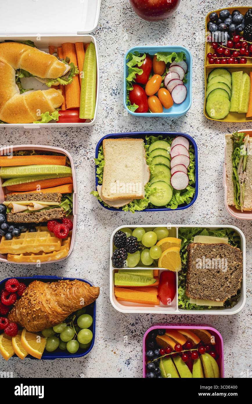 Aufnahme von Schullunchboxen mit verschiedenen gesunden, nahrhaften Mahlzeiten auf Steingrund, Draufsicht, flach liegend Stockfoto
