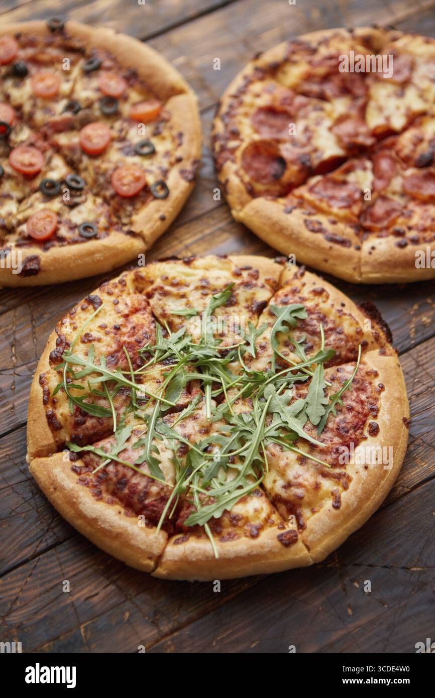 Komposition von drei verschiedenen Pizzen auf einem rostigen, zerkratzten Holztisch. Warme und frische Speisen, die verzehrfertig sind Stockfoto