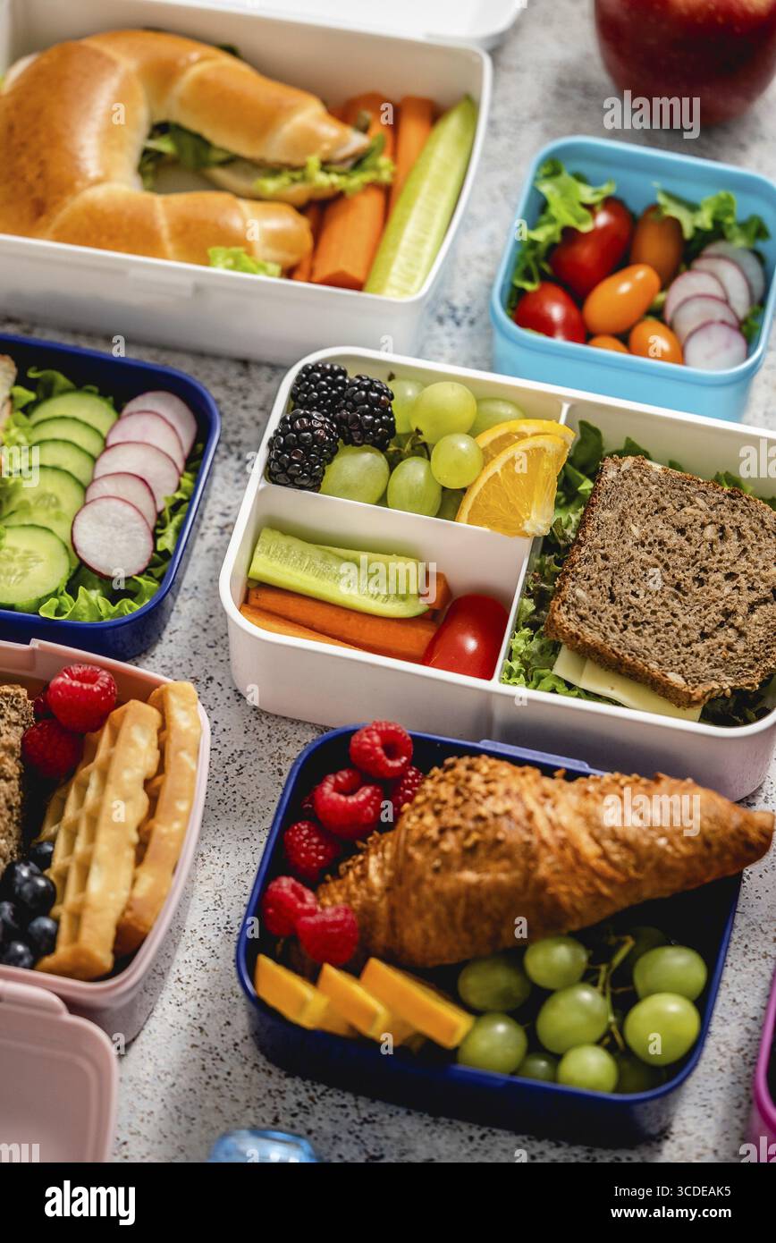 Aufnahme von Schullunchboxen mit verschiedenen gesunden, nahrhaften Mahlzeiten auf Steingrund, Draufsicht, flach liegend Stockfoto