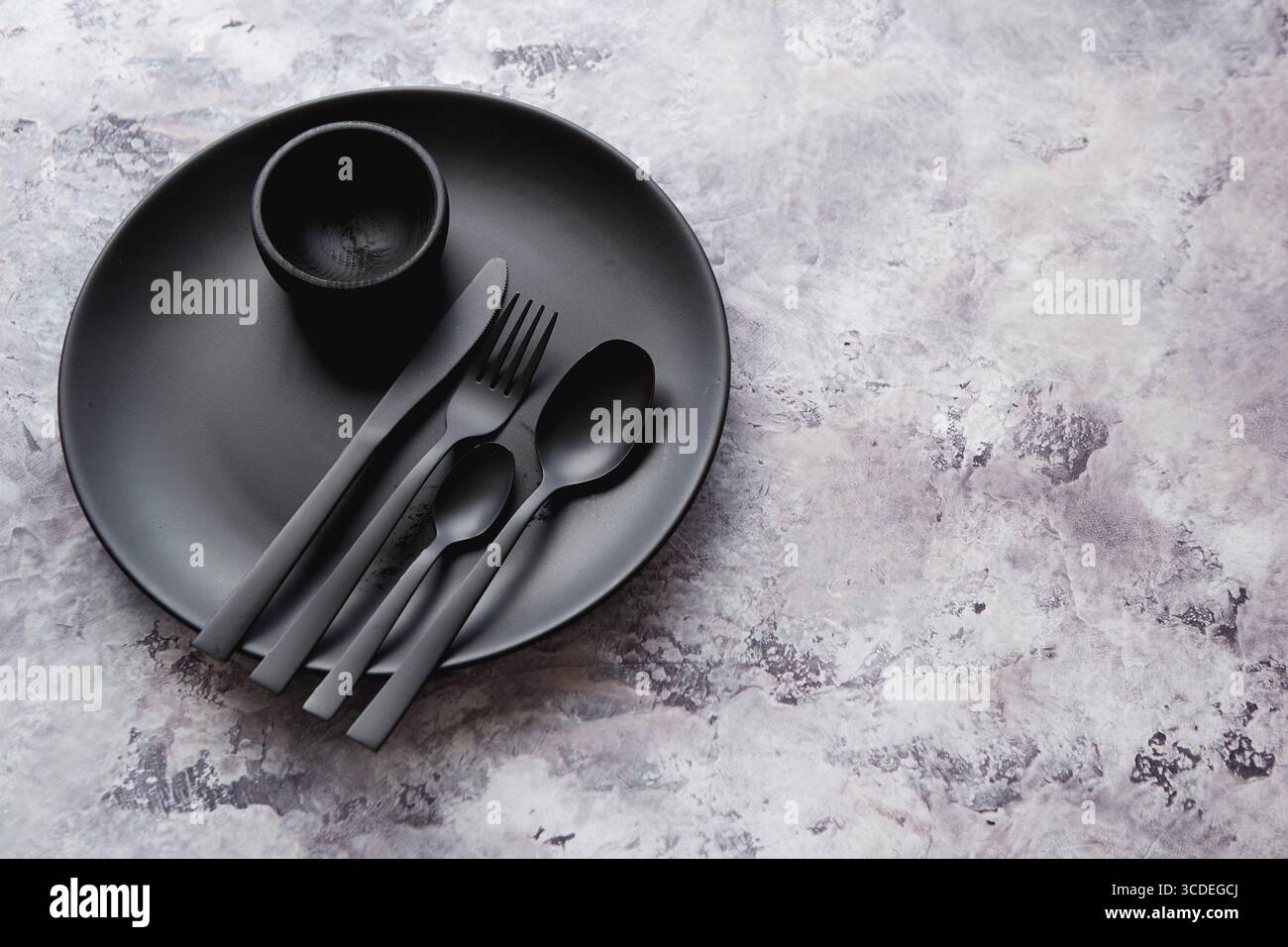 Blick von oben auf schwarzen leeren runden Teller und Geschirr auf Marmorstein Hintergrund Stockfoto