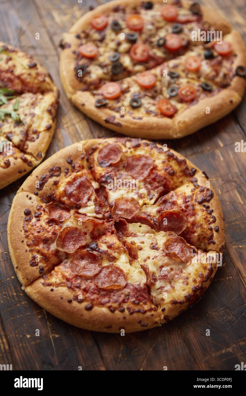 Komposition von drei verschiedenen Pizzen auf einem rostigen, zerkratzten Holztisch. Warme und frische Speisen, die verzehrfertig sind Stockfoto