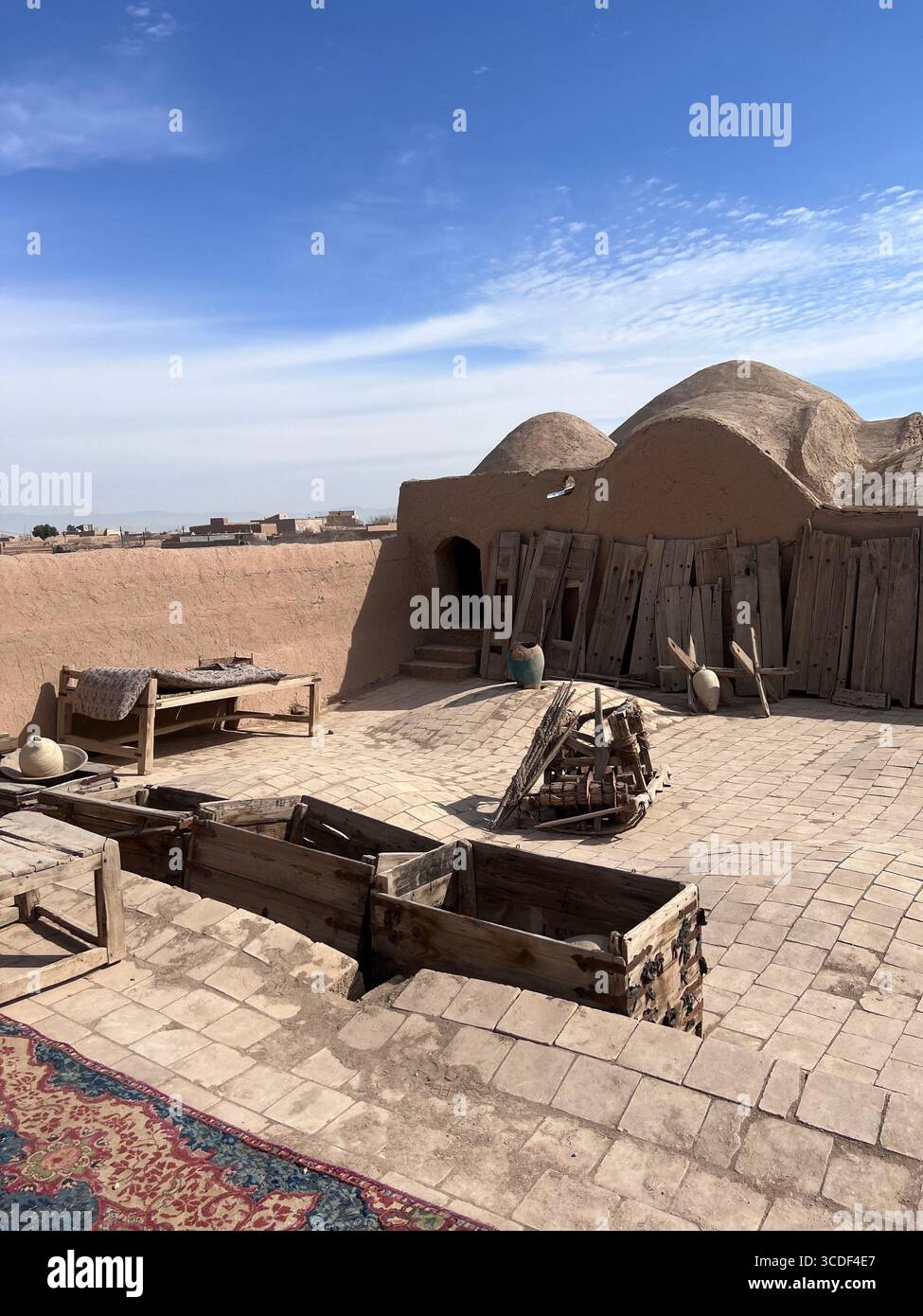 Lehm-Innenhof der Festung SAR Yazd mit Holzbänken, Töpferwaren und Kuppeldächern unter dem Wüstenhimmel. Stockfoto Lehm-Innenhof der Festung SAR Yazd mit Holzbänken, Töpferwaren und Kuppeldächern unter dem Wüstenhimmel. Stockfoto