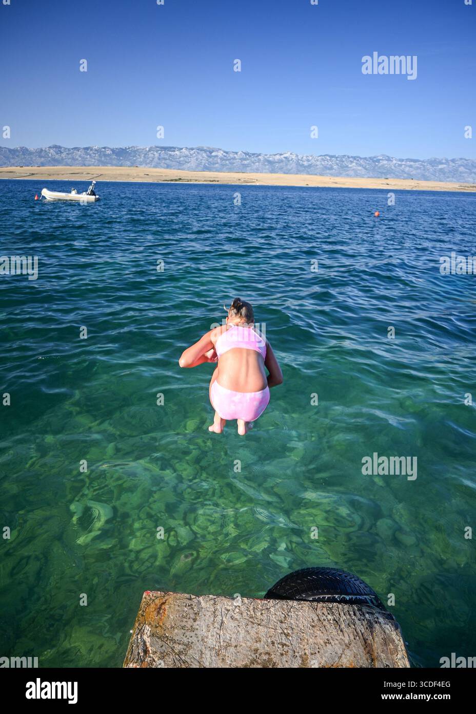 Ein junges Mädchen taucht von einem Steinpier in das transparente türkisfarbene Wasser der adria, Insel pag, kroatien. Stockfoto