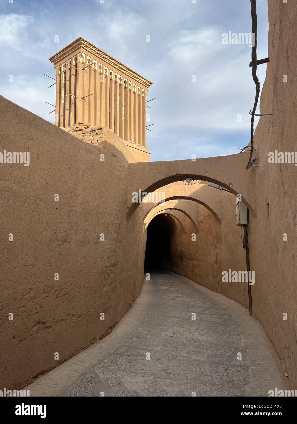 Eine schmale lehmgasse in Yazd, Iran, führt zu einem hohen traditionellen Windfänger vor dem blauen Himmel. Stockfoto Eine schmale lehmgasse in Yazd, Iran, führt zu einem hohen traditionellen Windfänger vor dem blauen Himmel. Stockfoto