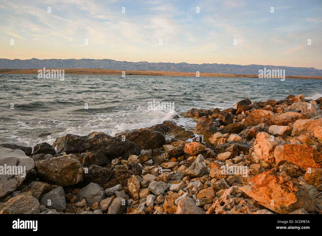 Malerischer Blick auf die Wellen, die an der Küste gegen Felsen plätschern, mit der velebit Bergkette im Hintergrund bei Sonnenuntergang. Stockfoto
