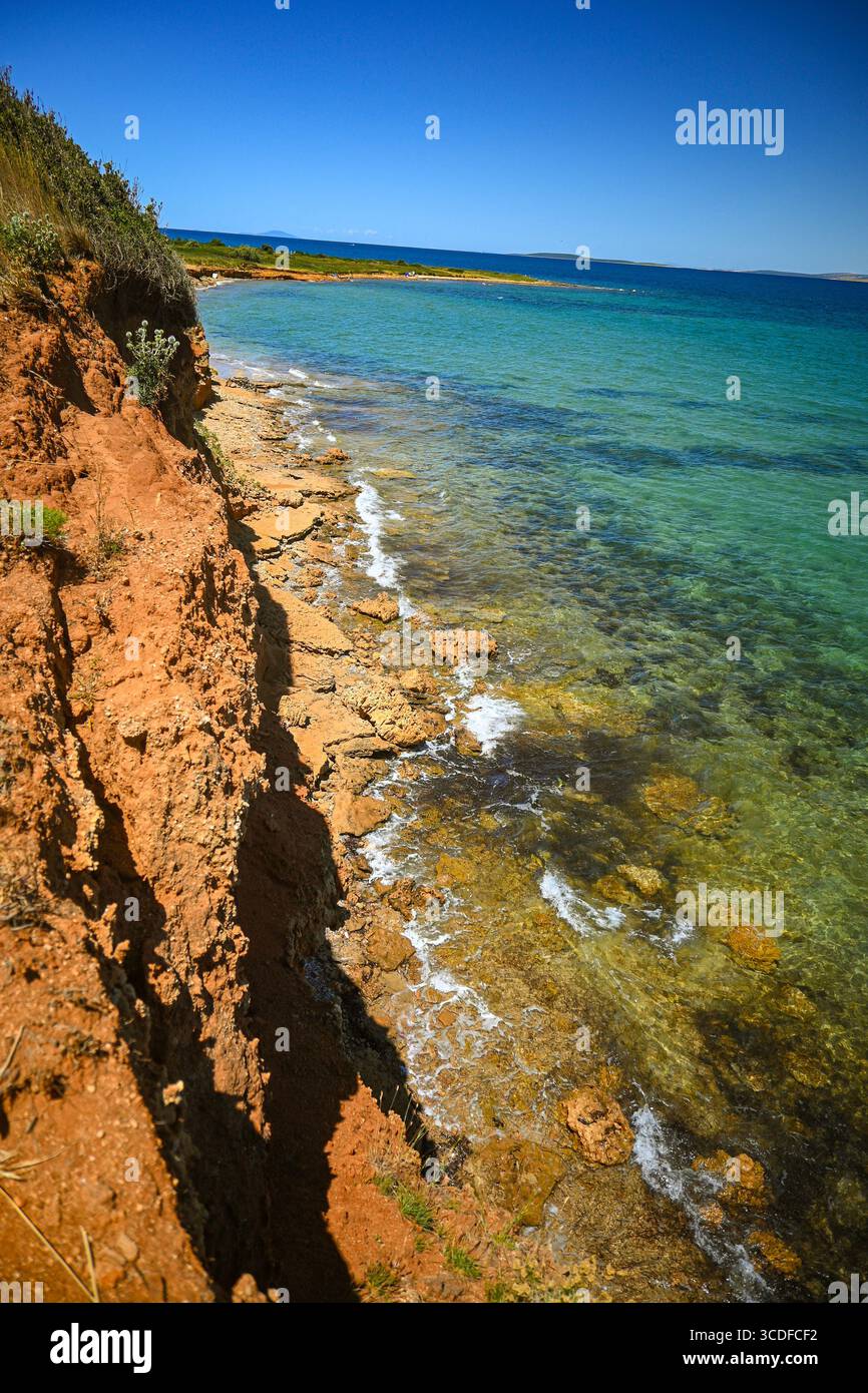 Wellen, die an sonnigen Sommertagen im mittelmeer sanft gegen die felsige Küste unter der roten Klippe schlagen. Stockfoto