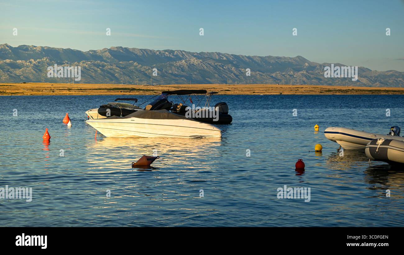 Weiße Motorboote und Jollen liegen bei Sonnenuntergang in ruhiger Bucht mit velebit-Bergen im Hintergrund. Stockfoto