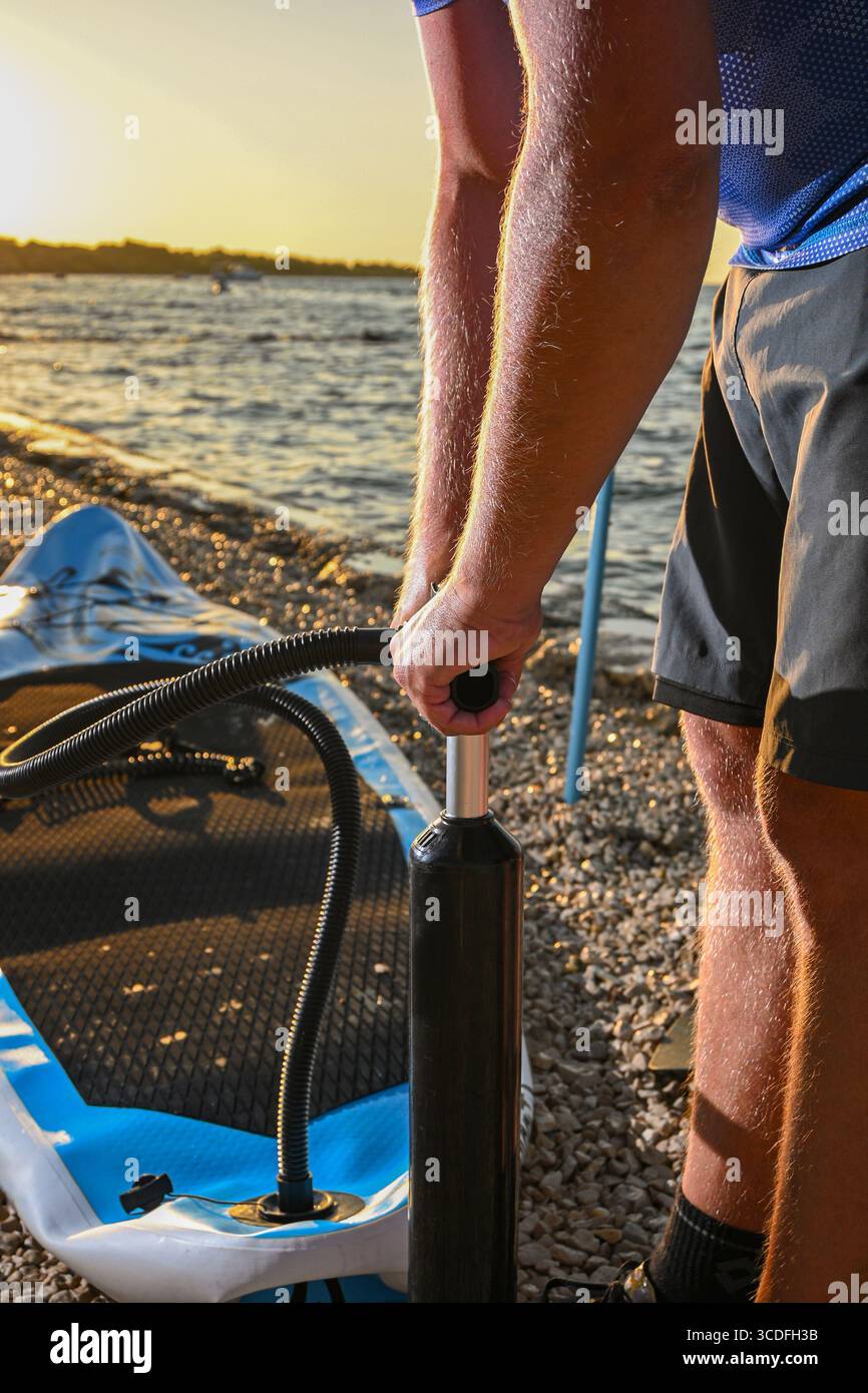Mann, der bei Sonnenuntergang an einem Kieselstrand mit Handpumpe aufbläst. Stockfoto