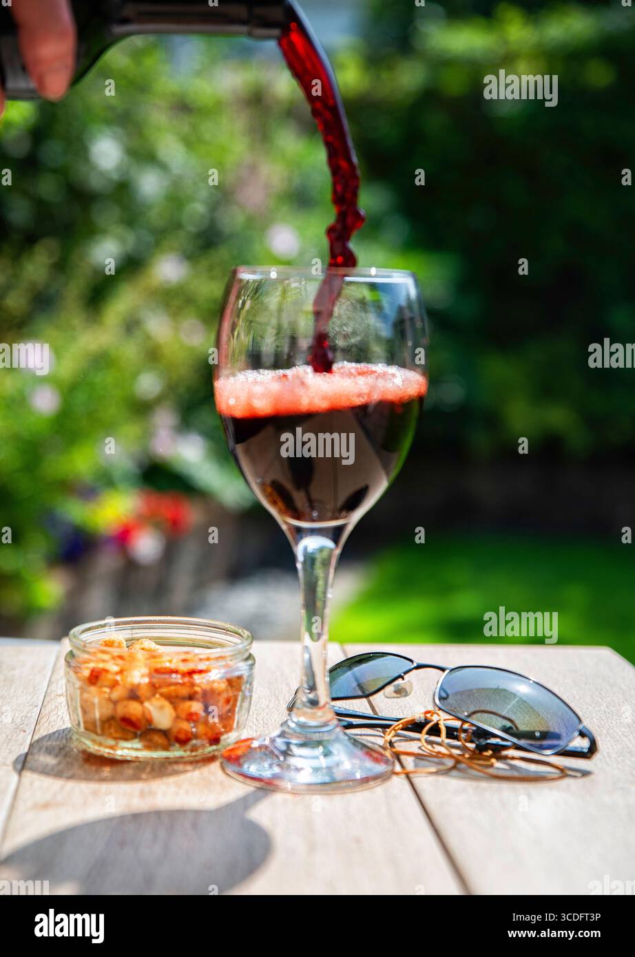 Ein Glas Rotwein wird in einem sonnigen Garten gegossen Stockfoto