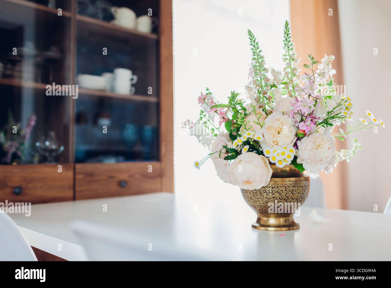 Nahaufnahme von Blumenarrangements in Messingvase auf Esstisch. Gemütlicher Wohnbereich mit Küche. Inneneinrichtung mit englischen Rosen Stockfoto