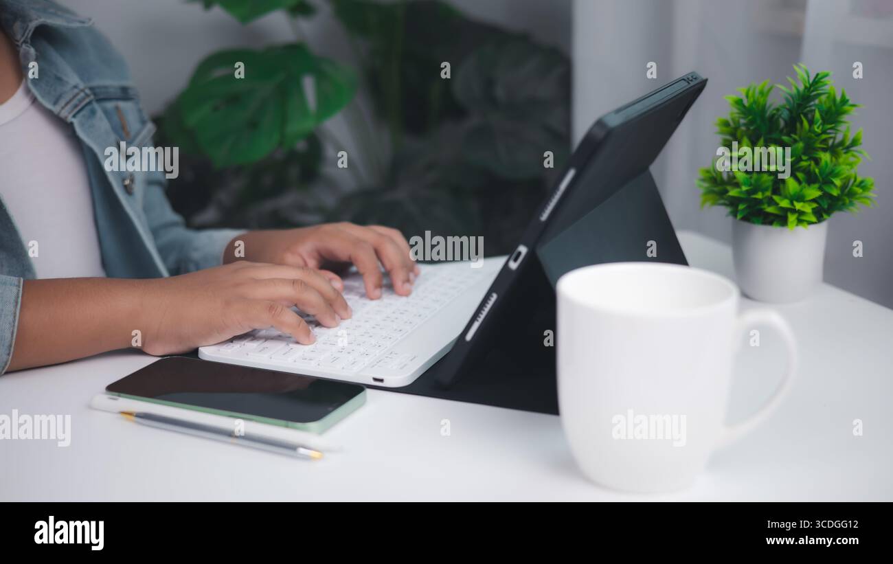 Moderne Fernarbeit, Freiberufung und digitale Produktivität. Helle, minimalistische Schreibtischeinrichtung mit Tablet und Tastatur, Smartphone, Stift und Kaffeetasse. Stockfoto