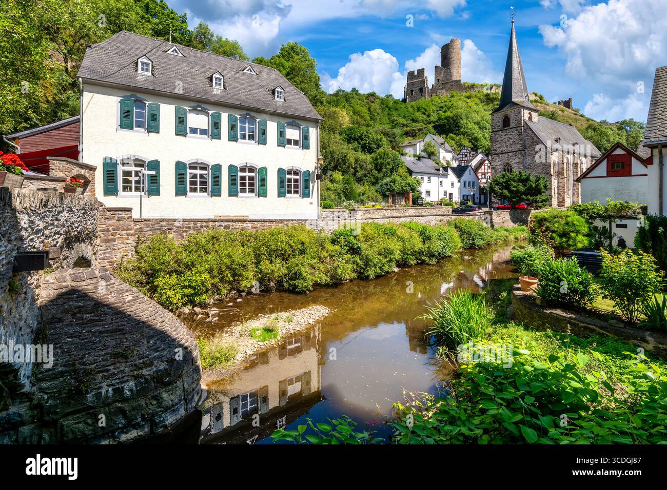 Historische Kirche in Monreal mit Blick auf die Löwenburg und den malerischen Fluss unter blauem Sommerhimmel Stockfoto