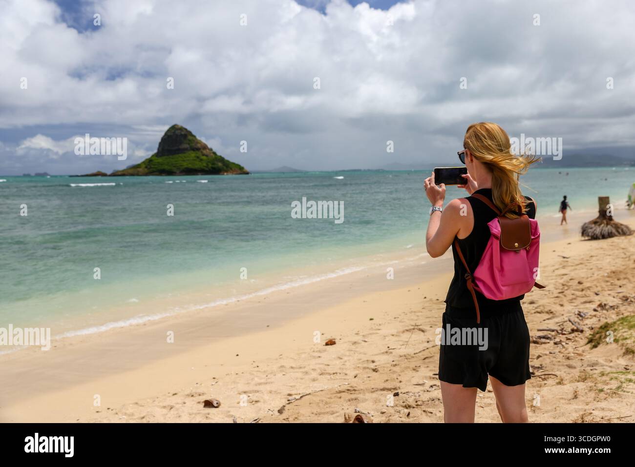 Eine Frau, die Fotos von Mokolii Island (auch Chinaman’s hat genannt) macht, die sich vor der Küste von Oahu, Hawaii, in der Nähe des Kualoa Regional Park befindet. Stockfoto