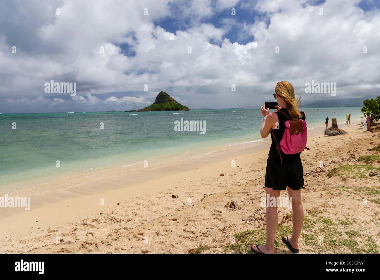 Eine Frau, die Fotos von Mokolii Island (auch Chinaman’s hat genannt) macht, die sich vor der Küste von Oahu, Hawaii, in der Nähe des Kualoa Regional Park befindet. Stockfoto