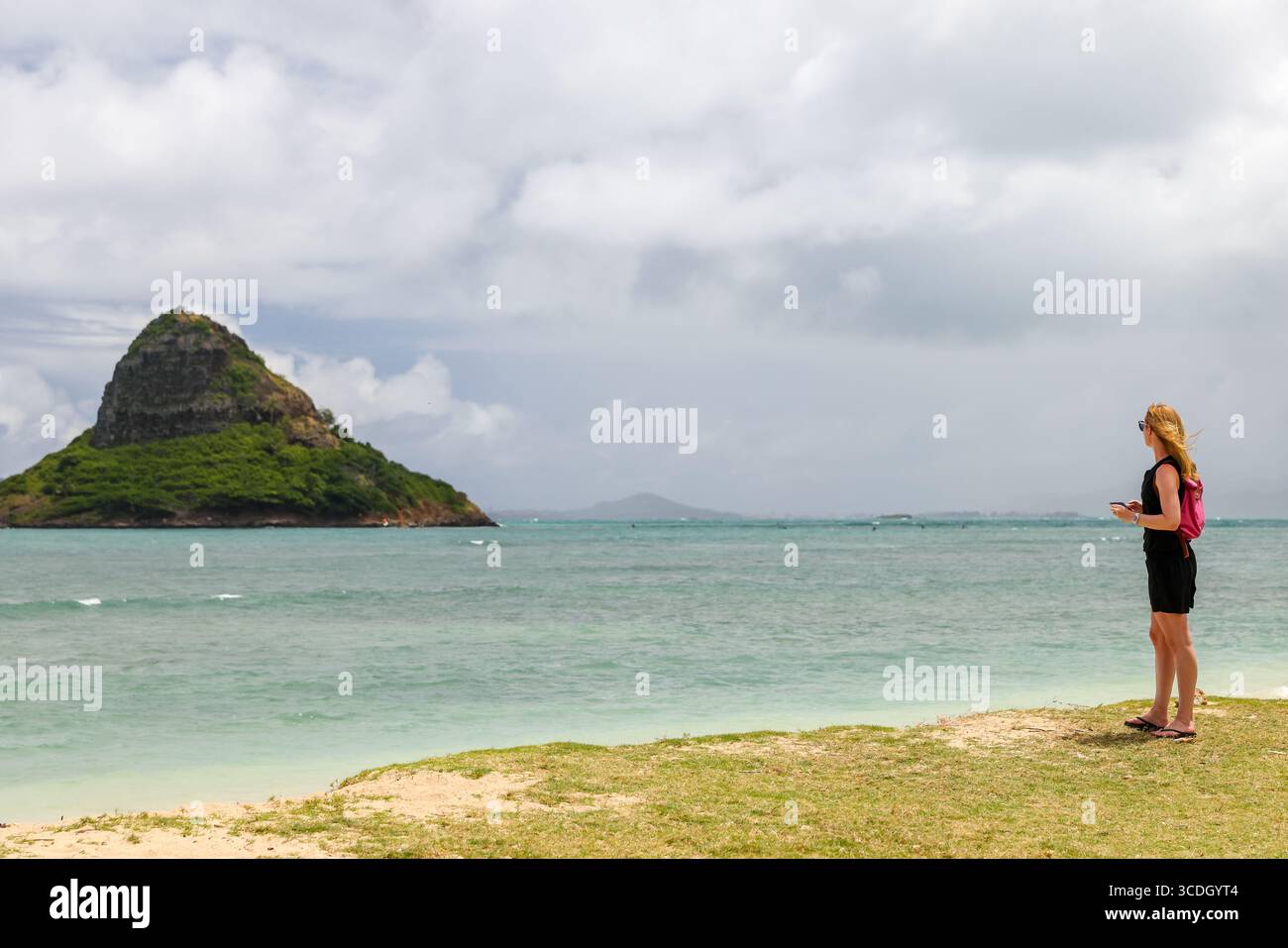 Eine Frau, die Fotos von Mokolii Island (auch Chinaman’s hat genannt) macht, die sich vor der Küste von Oahu, Hawaii, in der Nähe des Kualoa Regional Park befindet. Stockfoto