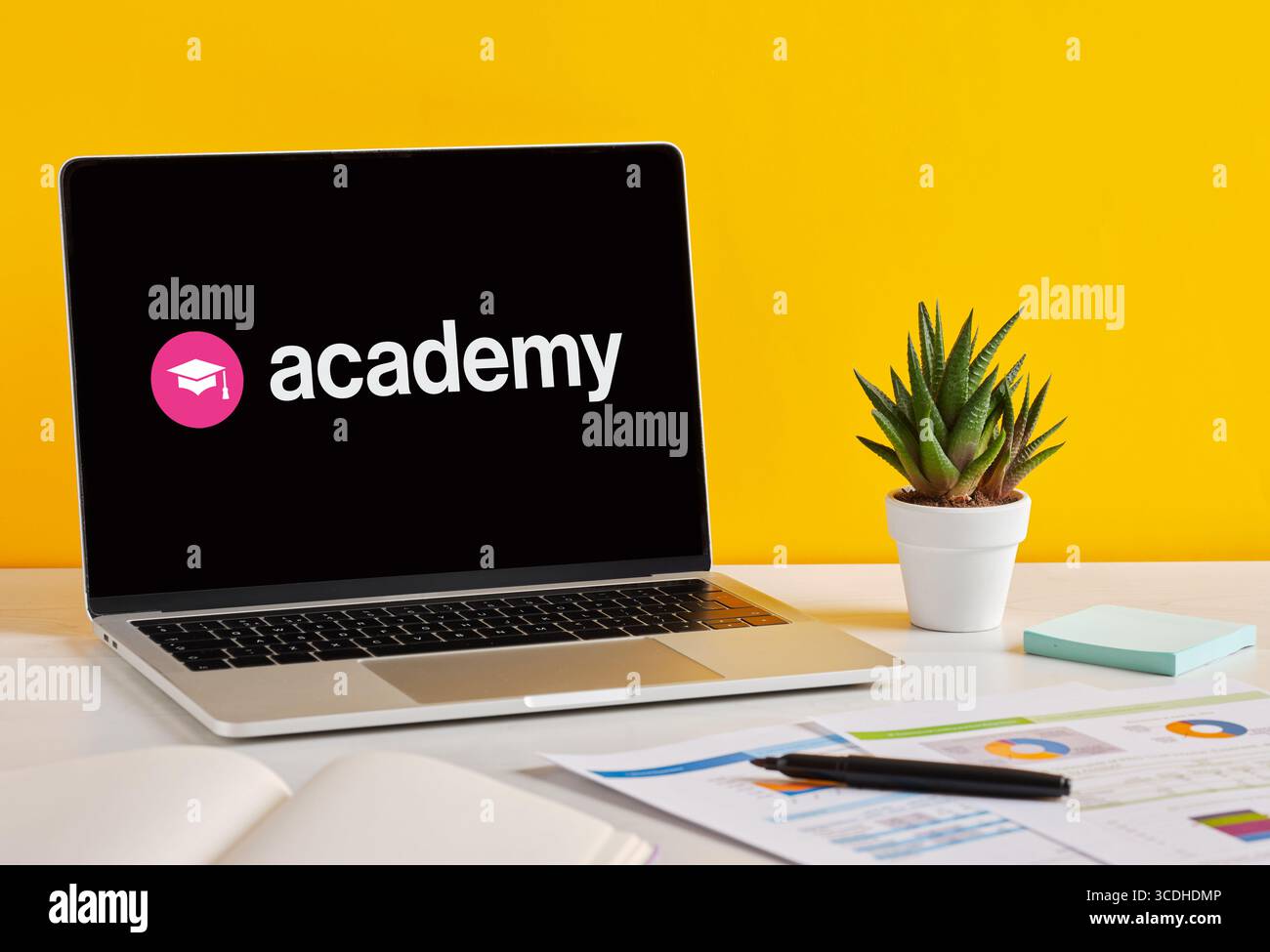 Academy-Logo auf dem Laptop-Bildschirm auf gelbem Hintergrund, das auf Online-Bildung und -Lernen hinweist. Stockfoto