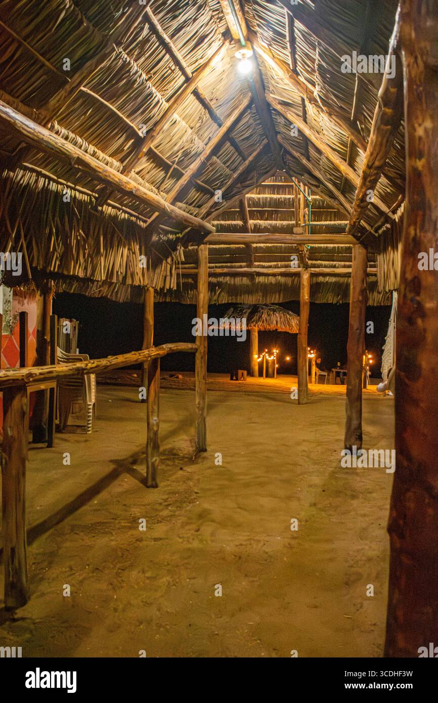 Innenansicht einer traditionellen Strohhütte in Cabo de la Vela mit Holzbalken und Ambiente-Beleuchtung in einer ruhigen Umgebung. Stockfoto