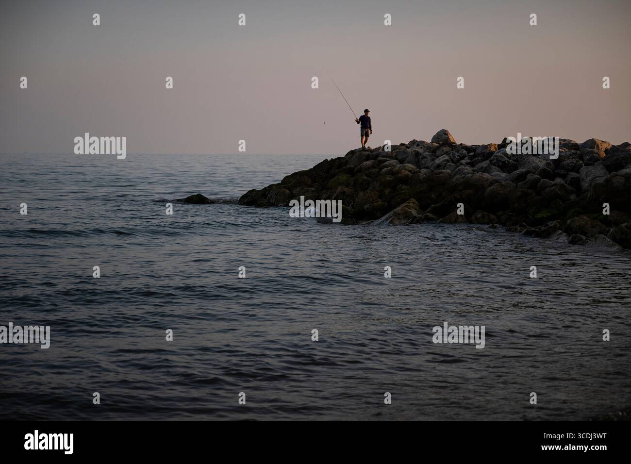 Einsamer Fischer mit Ruten in Händen, Silhouetten am Highcliffe Beach an der Südküste, kurz nach Sonnenuntergang Stockfoto