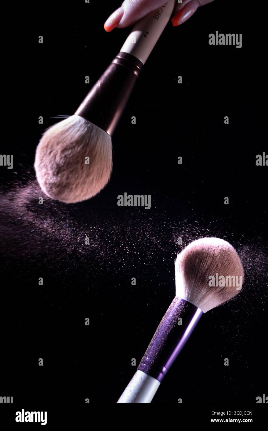 Zwei Make-up-Pinsel vor dunklem Hintergrund, mit einer Streuung von etwas, das wie Kosmetikpulver oder Pigment aussieht Stockfoto