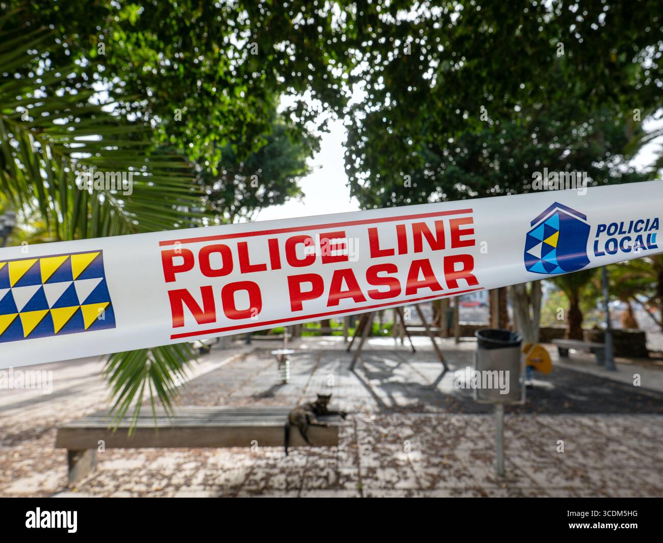 Polizeiband mit der Aufschrift „POLIZEILINIE NICHT ÜBERQUEREN“ in einem Park auf den Kanarischen Inseln. Bäume und Vegetation sind hinten sichtbar. Stockfoto