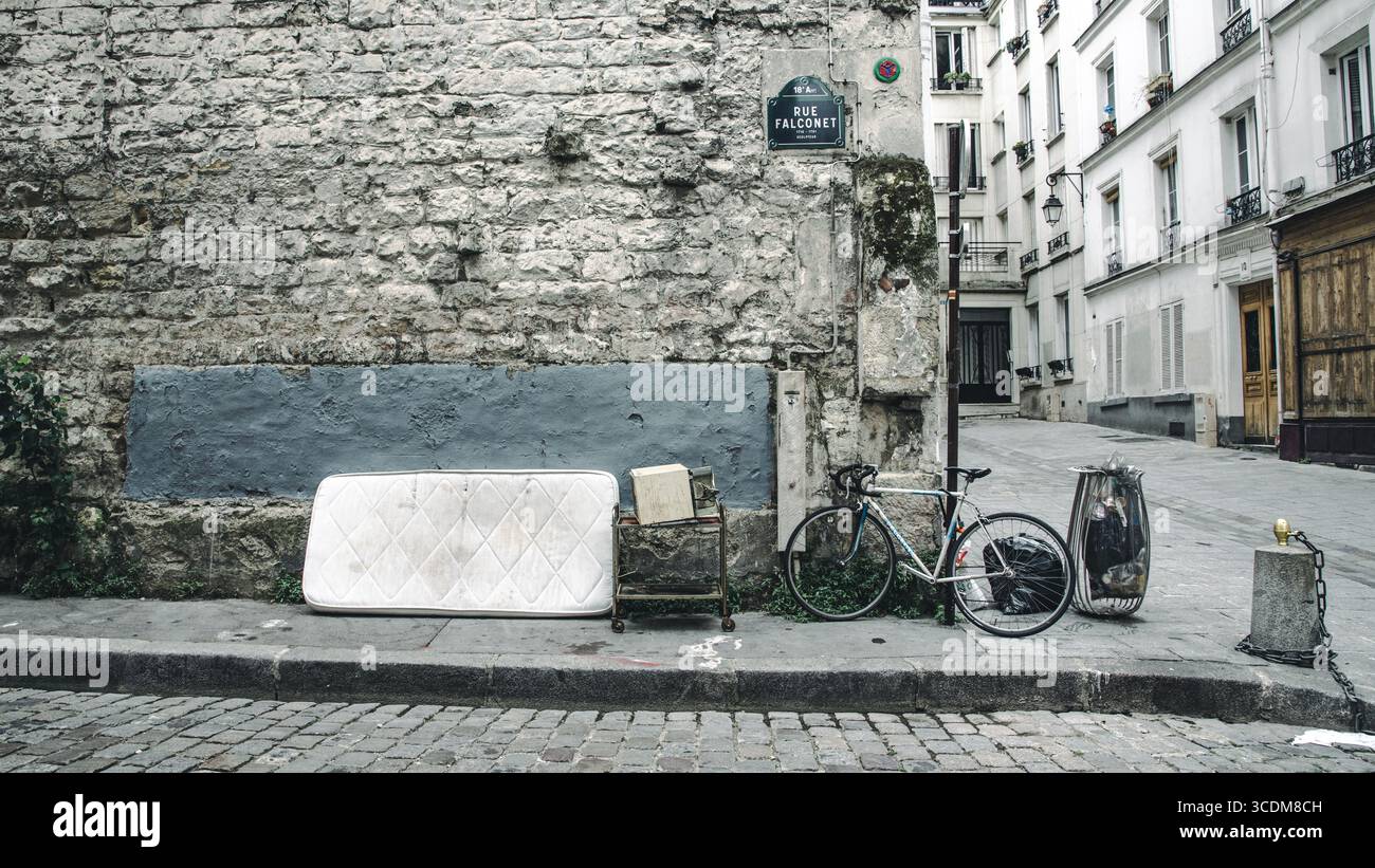 Materasso abbandonato accanto a bicicletta e muro in pietra in una strada di Parigi, fotografia urbana in bianco e nero dal tono editoriale. Stockfoto