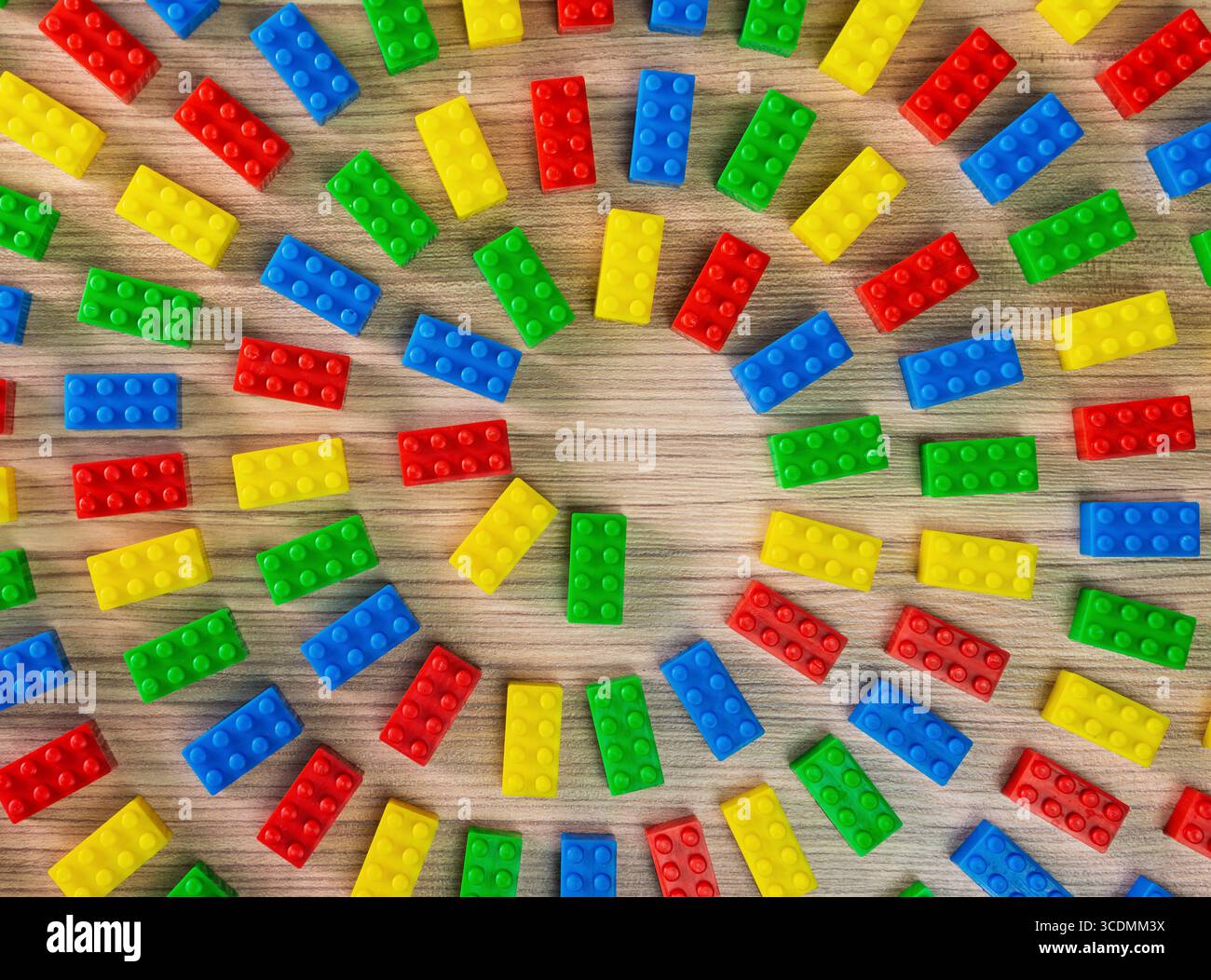 Eine kreative flache Lage aus bunten Spielzeugziegeln, die in einem kreisförmigen Muster auf einem hölzernen Hintergrund angeordnet sind. Stockfoto
