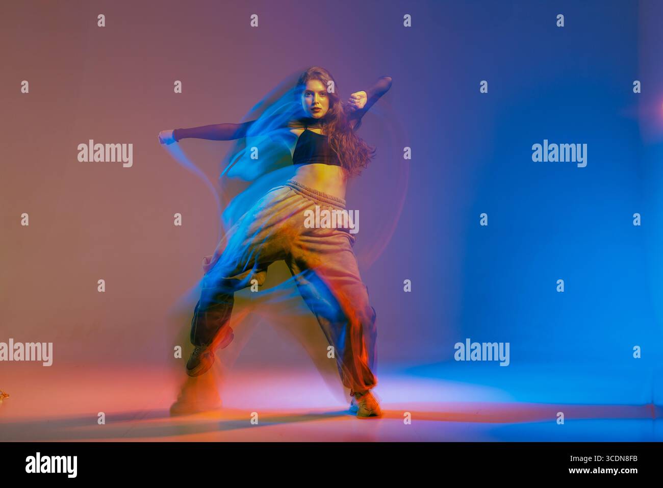 Selbstbewusste Jazz-Funk-Tänzerin im modernen urbanen Stil mit ausdrucksstarker Choreografie mit dynamischer farbenfroher Beleuchtung. Stockfoto