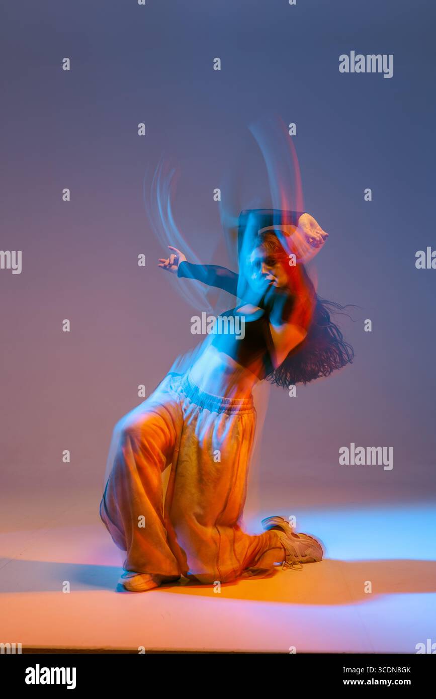 Stilvolle Jazz-Funk-Tänzerin mit dynamischer Choreografie mit lebendiger Beleuchtung und starker urbaner Energie in kreativer moderner Tanzposition. Stockfoto